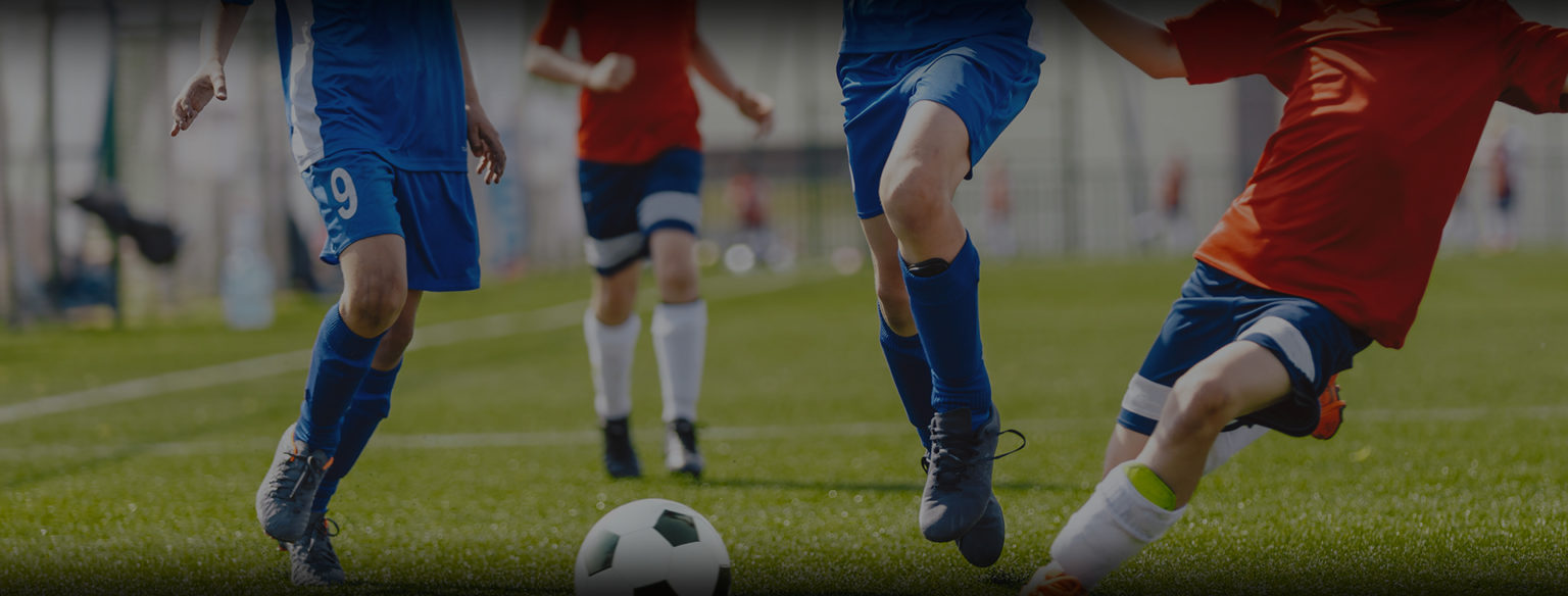 Youth soccer players in blue and red custom kits chasing a classic black and white soccer ball.