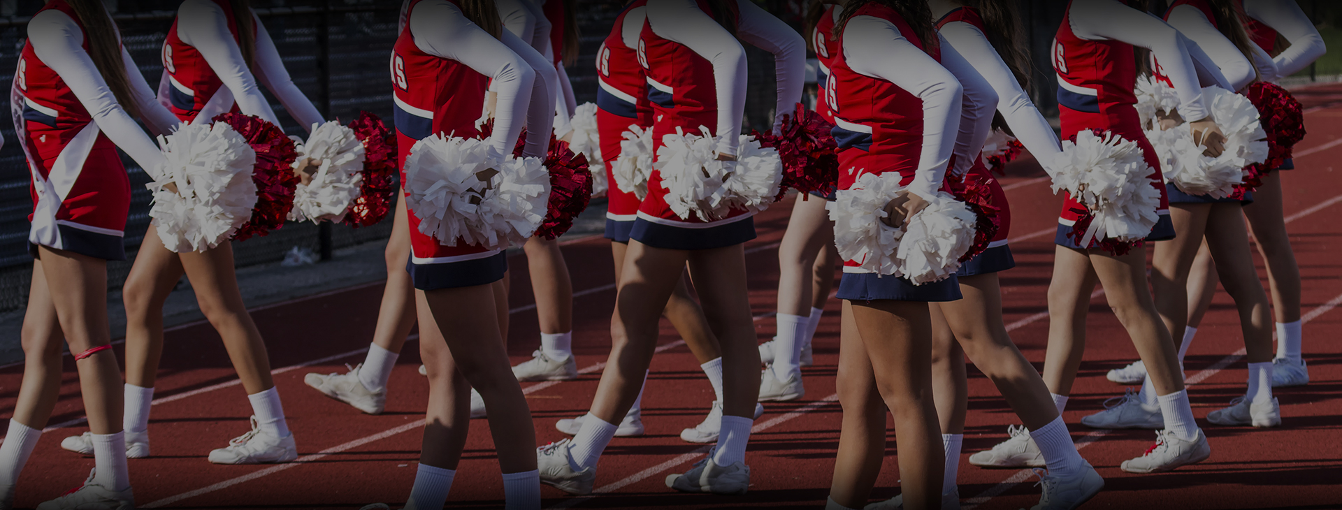 Cheerleaders in red, white, and blue custom uniforms marching in formation holding pom-poms on a track.
