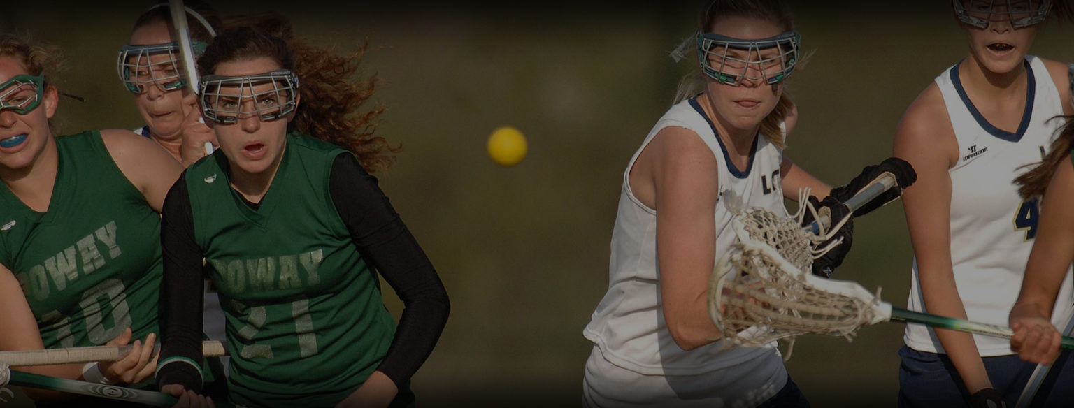 Female lacrosse players in green and white team uniforms competing with lacrosse sticks on the field.
