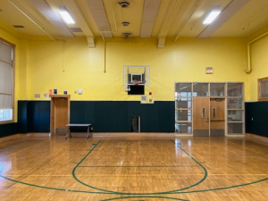 Custom dark green gym wall padding installed along the back wall of a yellow high school basketball gymnasium.