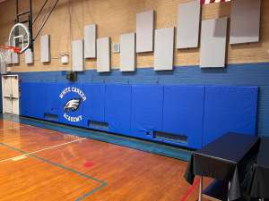 Side angle of custom blue gym wall padding with printed White Career Academy eagle logo on a basketball court wall.
