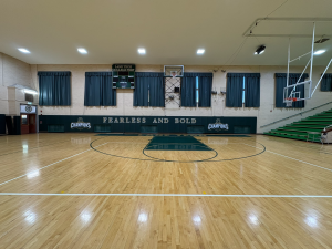 Green athletic wall padding printed with Fearless and Bold text and Champions logos in a basketball gym.